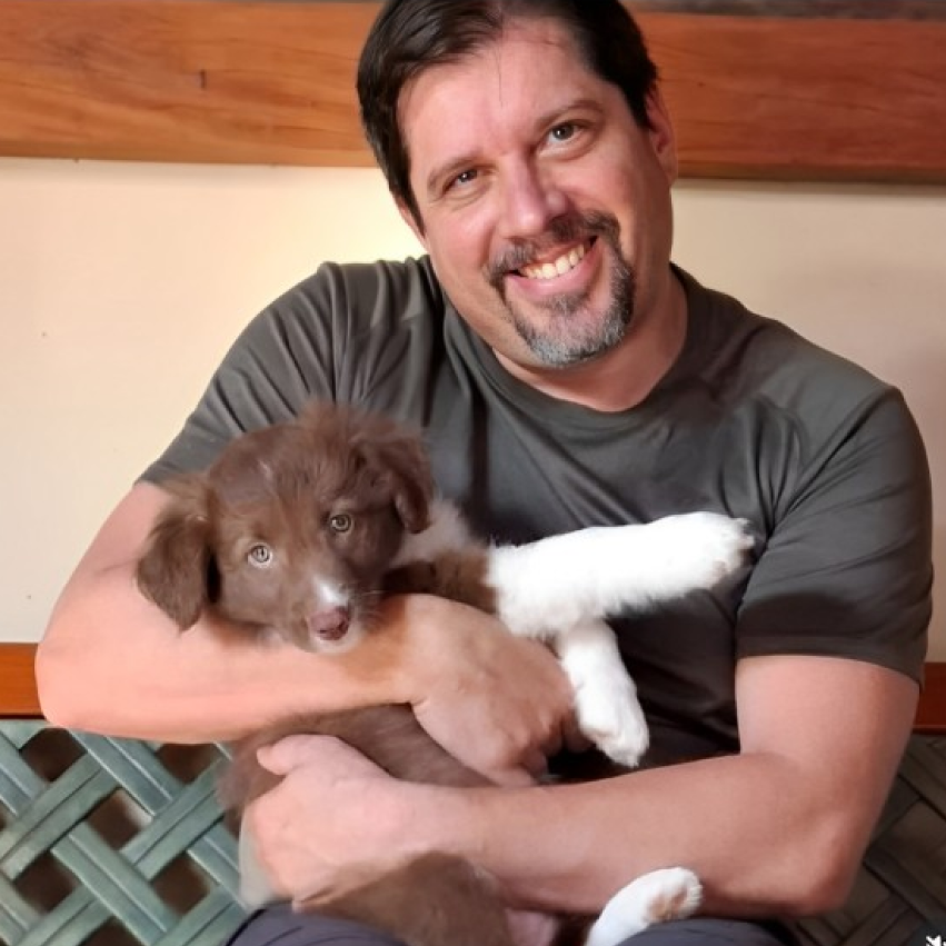 Leandro Ledel abraçando seu cachorro, o animal é marrom com as patas brancas
